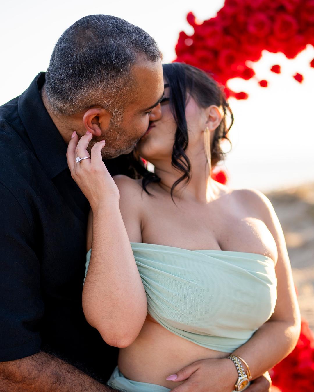 Couple kissing just after the proposal, red roses behind them